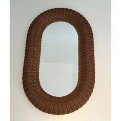 a brown wicker oval mirror hanging on the wall next to a toilet paper dispenser