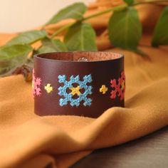 a brown leather bracelet with crocheted flowers on the side and a green plant in the background