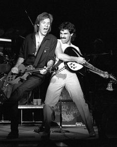 two men playing guitars on stage with one holding the other's leg up in front of him