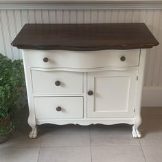 a white dresser with brown top in a room next to a potted green plant