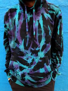 a man standing in front of a blue wall wearing a black and purple tie dye hoodie