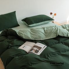 a bed with green sheets and pillows on top of it, next to a book