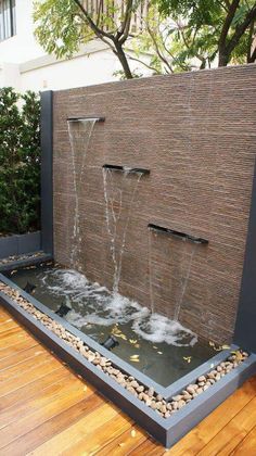 an outdoor fountain with water coming out of the top and side walls, surrounded by wooden flooring