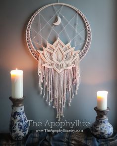 two candles are sitting on a table next to a wall hanging with a dream catcher