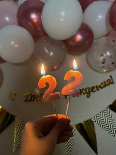 someone is holding two candles with the number twenty on them in front of some balloons