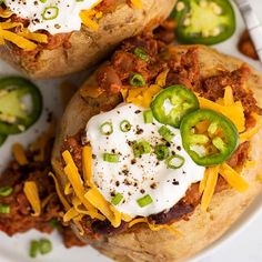 two stuffed potatoes topped with chili cheese and jalapenos on a white plate