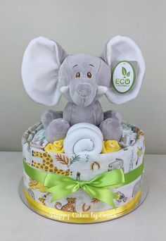 a baby elephant sitting on top of a diaper cake with green ribbon around it