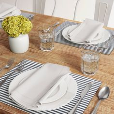 the table is set with white plates, silverware and flowers in glass vases