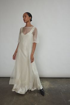 a woman standing in front of a white wall wearing a dress with sheer sleeves and black shoes