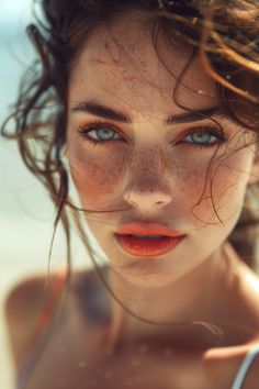 a woman with freckled hair and blue eyes looks into the camera while standing on the beach