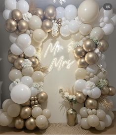 a white and gold balloon arch with balloons on the wall, flowers and greenery