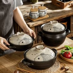 two pots with fish designs on them sitting on a wooden table next to some vegetables