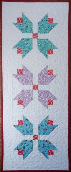 a quilted wall hanging with blue and red birds on it's sides, in the shape of arrows