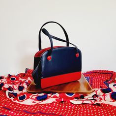 Vintage blue and red colorblocked faux leather top handle handbag or shoulder bag in a mod 60s style. Has two outer pockets, the inner main pocket, and a hidden inner pocket with a metal zipper. The inner pocket closes with a metal clasp. No brand markings.  Condition: No wear to the bottom, straps, zippers, or lining, but 2 of the 4 decorative buttons have small discolored scuffs.  10 inches wide,  3.5 inches deep,  8 inches tall without the strap,  Strap is 6 inches from top of purse to the mi Retro Red Top Handle Satchel, Retro Red Bags With Handles, Retro Top Handle Box Bag For Shopping, Retro Red Bag With Top Carry Handle, Retro Red Top Handle Shoulder Bag, Red Retro Top Handle Shoulder Bag, Retro Red Satchel With Detachable Handle, Retro Red Satchel With Detachable Strap, Red Retro Satchel With Detachable Strap