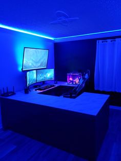 a room with blue lighting and two computer screens on the desk in front of it