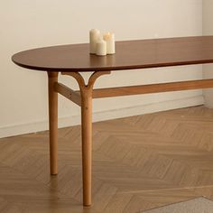 a table with two candles on it in front of a white wall and wooden floor