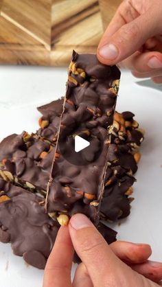 two hands reaching for a piece of chocolate covered doughnut with nuts on the top