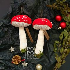 two red mushrooms with white dots on them sitting next to christmas ornaments and greenery