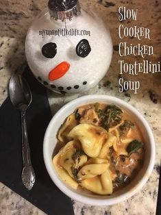 a bowl of tortellini soup next to a snowman ornament