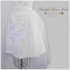 "This white cotton bridal bow belt comes in two styles, the Mini Bow and the Classic Bow. Each style comes with a 29\" long removable tulle train. The belt is also made with a partial elastic band for comfort and a hidden hook-and-eye closure. Perfect for a bridal shower, Vegas wedding, bachelorette and more. DRESS NOT INCLUDED. CLASSIC BOW BELT 1\" (band width) 4\" x 6\" (bow) MINI BOW BELT 1\" (band width) 1\" x 3\" bow) WOMENS: XS (25\"), S (27\"), M (29\"), L (31\"), XL (34\"), waistband. CU Fitted Bridal Belt With Ribbon For Wedding, Satin Bridal Belt With Ribbon For Wedding, Bridal Belt Ribbon, Elegant White Bridal Belt With Ribbon, White Fitted Bride Sash, Fitted White Lace Bridal Belt, Bridal Bow, Tulle Train, Mini Bow