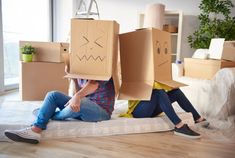 two people sitting on the floor with cardboard boxes in front of their heads and faces