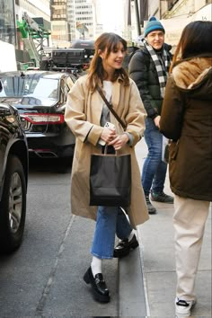 a woman is walking down the street carrying a black bag and smiling at someone behind her