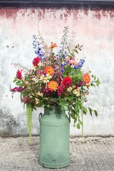 a green bucket filled with lots of colorful flowers on top of a cement floor next to a wall