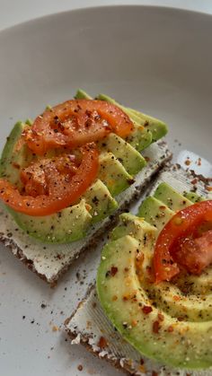 avocado toast with tomato slices and seasoning on the top, sitting on a white plate