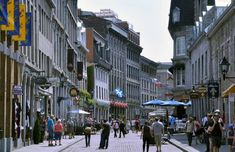 many people are walking down the street in an old city with tall buildings on both sides