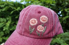 a pink hat with flowers embroidered on the front and side, in front of some trees