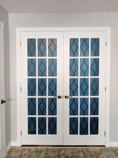 two glass doors with decorative designs on them in a white walled entryway to a home