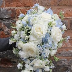 a bridal bouquet with white and blue flowers on a brick wall in front of a brick building