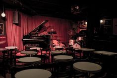 a room filled with lots of tables and chairs next to a piano in front of a red curtain