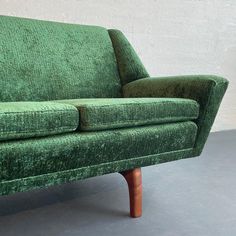 a green couch sitting on top of a gray floor next to a wooden leg chair