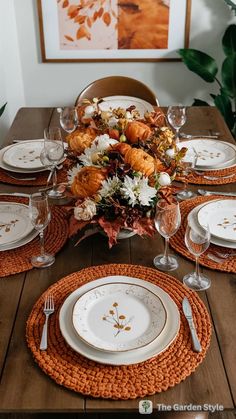 the table is set with white plates and orange napkins, silverware and flowers