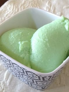 two scoops of green ice cream sitting in a bowl on a white tablecloth