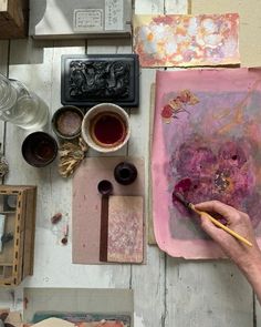 a person is painting on a piece of paper with watercolors and paintbrushes