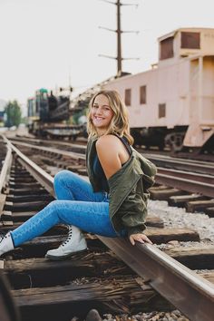 a woman sitting on train tracks with her legs crossed and looking at the camera while smiling