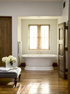 a large white bath tub sitting next to a wooden door in a bathroom on top of a hard wood floor