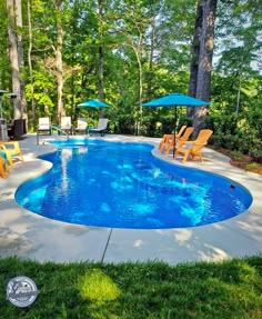 an empty swimming pool with lawn chairs and umbrellas in the background, surrounded by trees