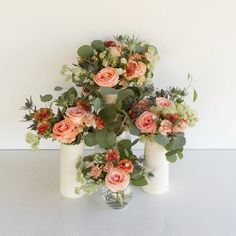 three vases filled with flowers and greenery on a white counter top next to each other