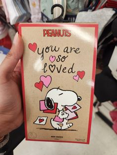 a person holding up a card with peanuts on it that says, you are so loved