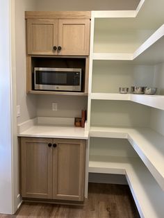 a kitchen with white shelving and wood flooring in the corner, including a microwave oven