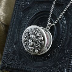 "Locket: Created from original Art Nouveau metal dies circa 1905. Beautiful stylized image is embossed in relief, and accented with three crystals. Fits two photos. Chain: Slinky high quality double rope Hand burnished silver Locket: 1-1/4\" Chain: 17\" Created and produced in our Los Angeles studio" Ornate Medallion Jewelry, Ornate Medallion Stamped Jewelry, Antique Silver Victorian Keepsake Necklace, Victorian Antique Silver Stamped Jewelry, Antique Silver Stamped Victorian Jewelry, Victorian Style Stamped Antique Silver Jewelry, Ornate Engraved Locket Necklace Vintage Collection, Antique Silver Victorian Necklace For Keepsake, Victorian Antique Silver Necklace For Keepsake