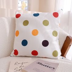 a polka dot pillow sitting on top of a white couch next to a book and magazine