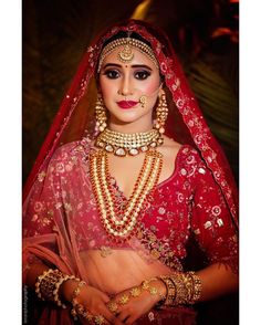 a woman wearing a red and gold bridal outfit with jewelry on her head, in front of a dark background