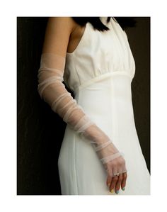 a woman in a white dress with her hand on the back of her arm wearing a pair of gloves