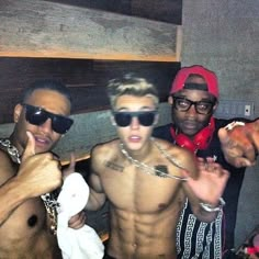 three shirtless men posing for the camera in front of a wall with chains on it