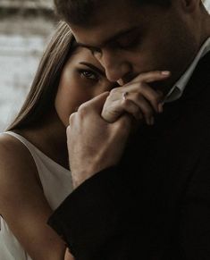 a man and woman standing next to each other in front of a body of water