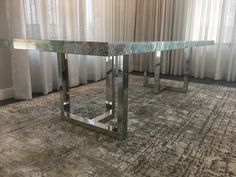 a glass and metal table in front of curtains